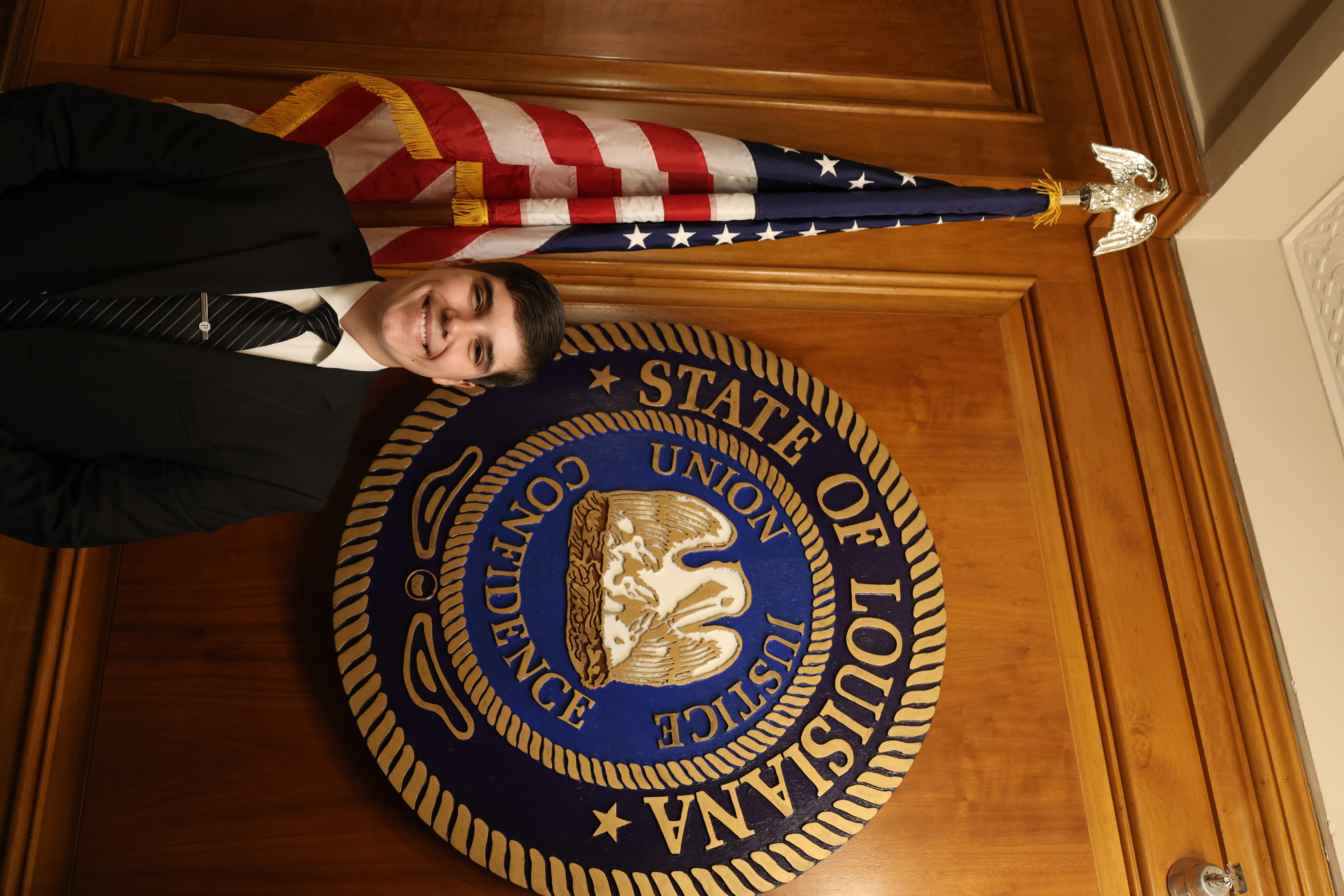 Headshot of boy in front of the Louisiana State symbol and American Flag