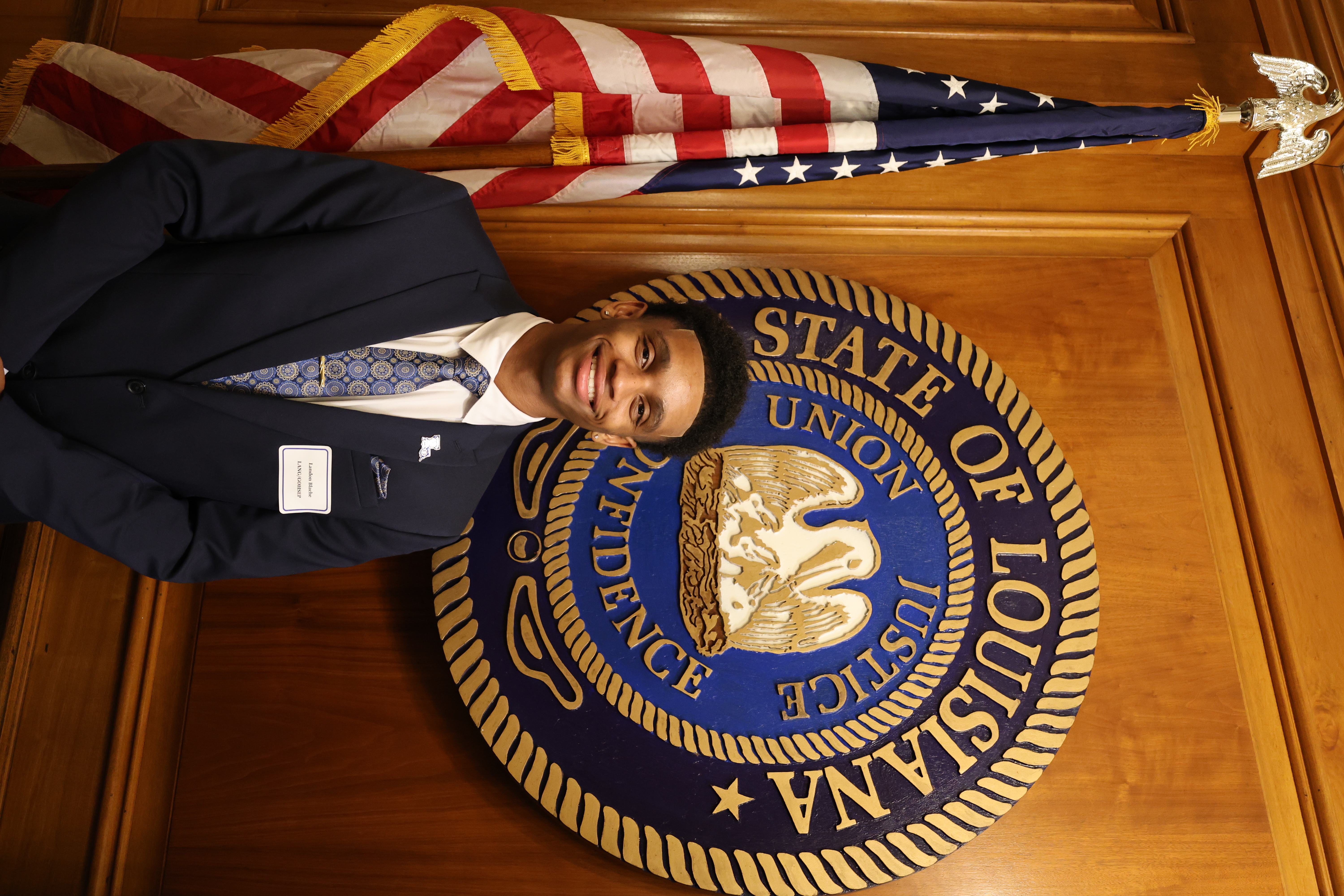 Headshot of boy in front of the Louisiana State symbol and American Flag