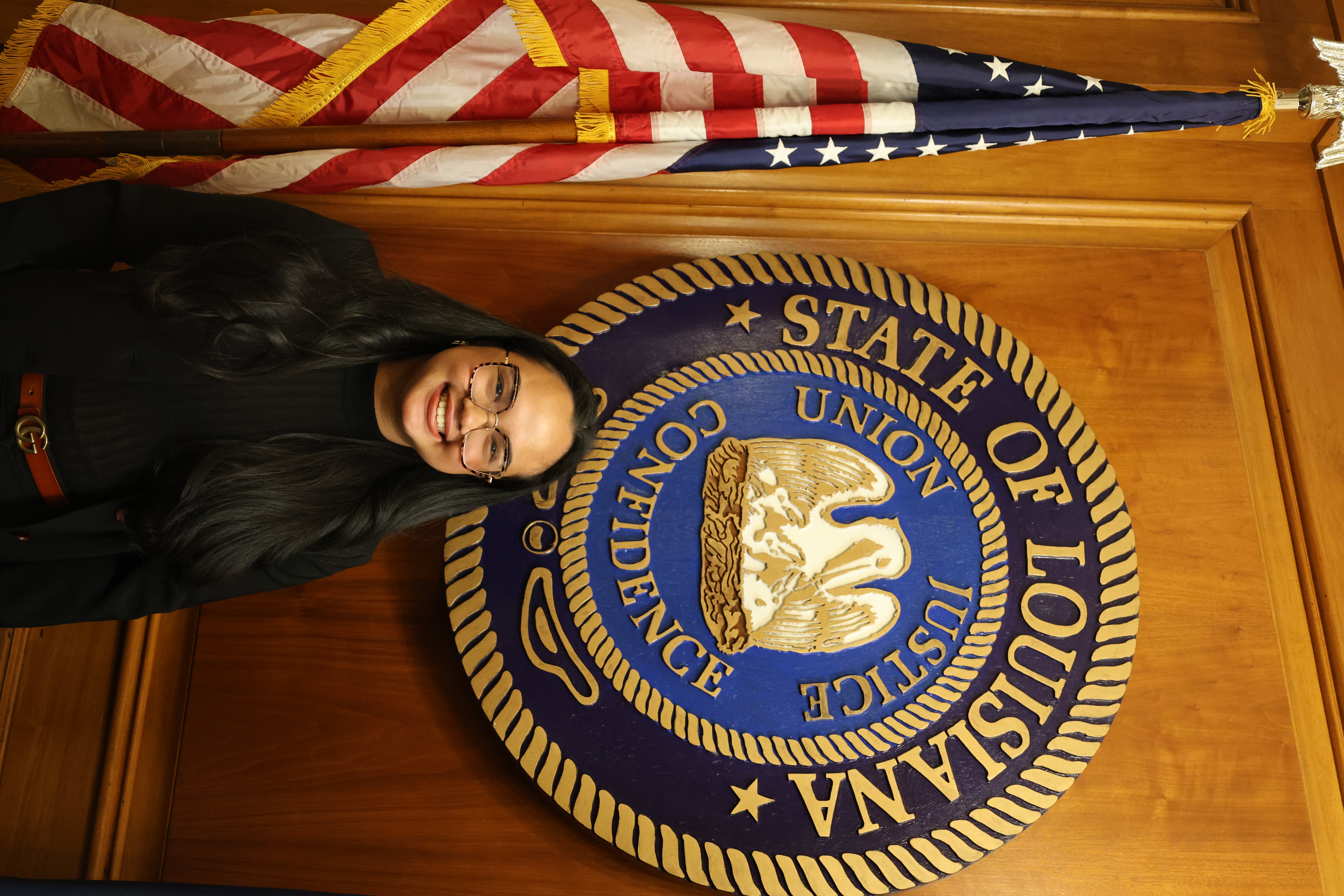 Headshot of girl in front of the Louisiana State symbol and American Flag