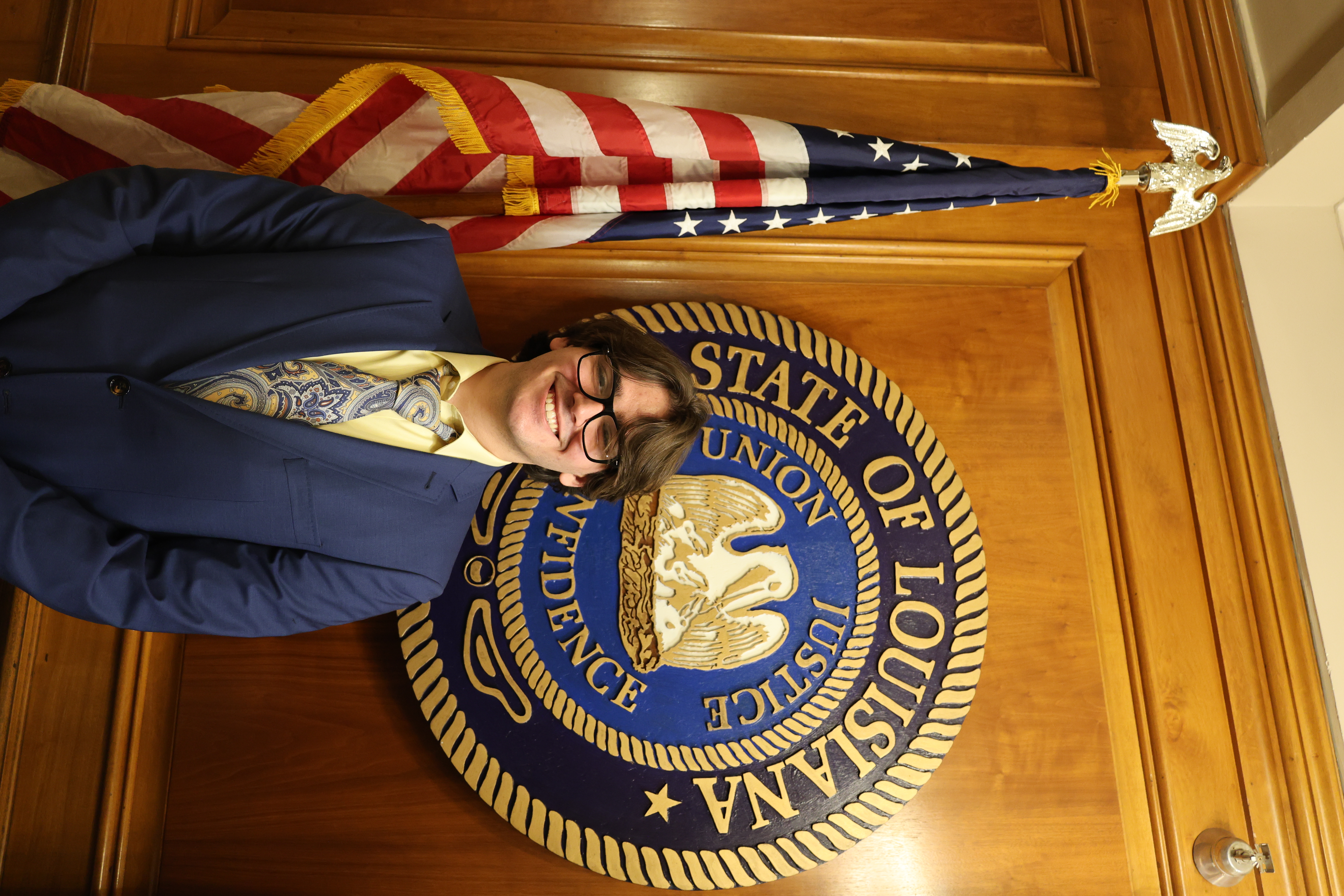 Headshot of boy in front of the Louisiana State symbol and American Flag