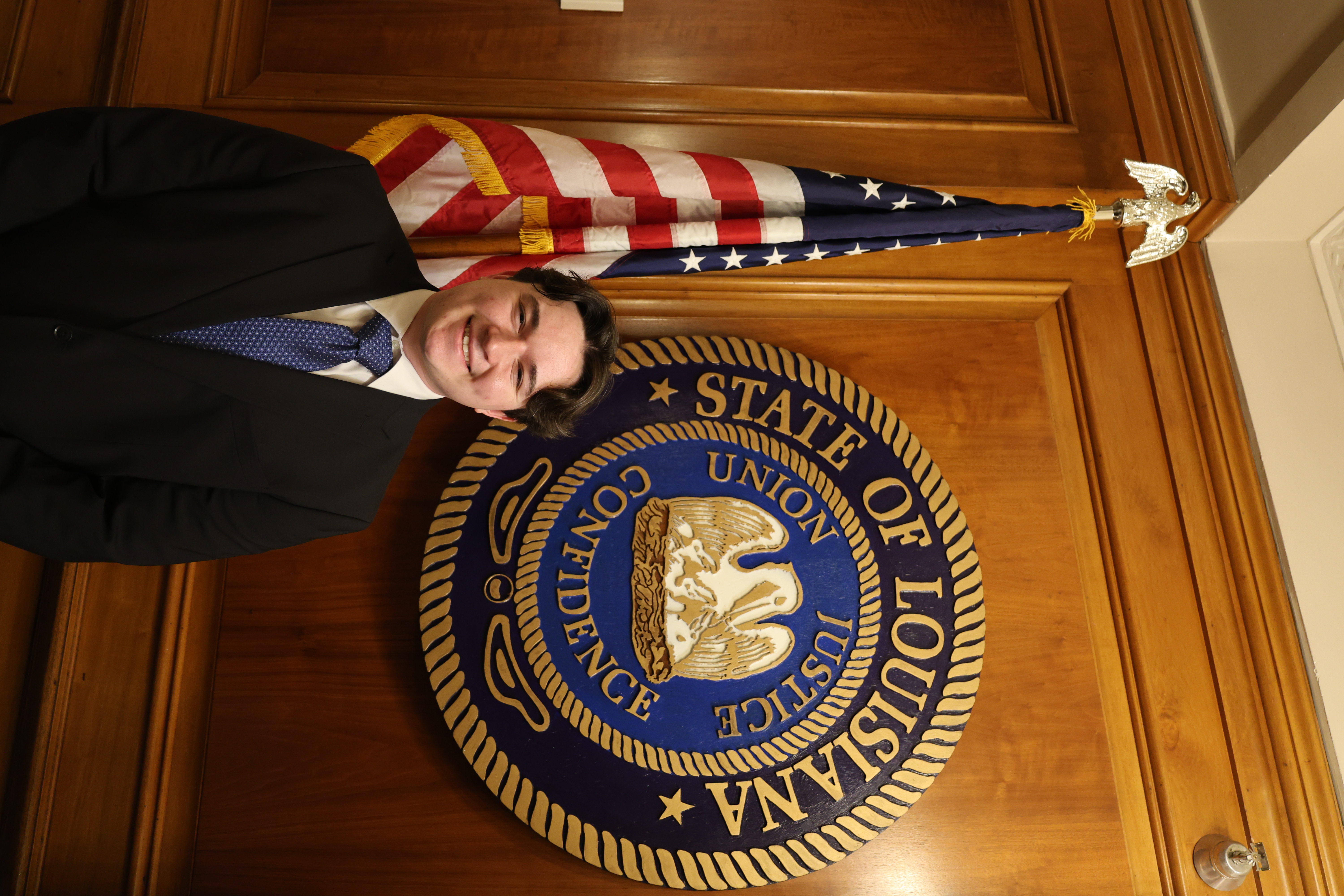 Headshot of boy in front of the Louisiana State symbol and American Flag